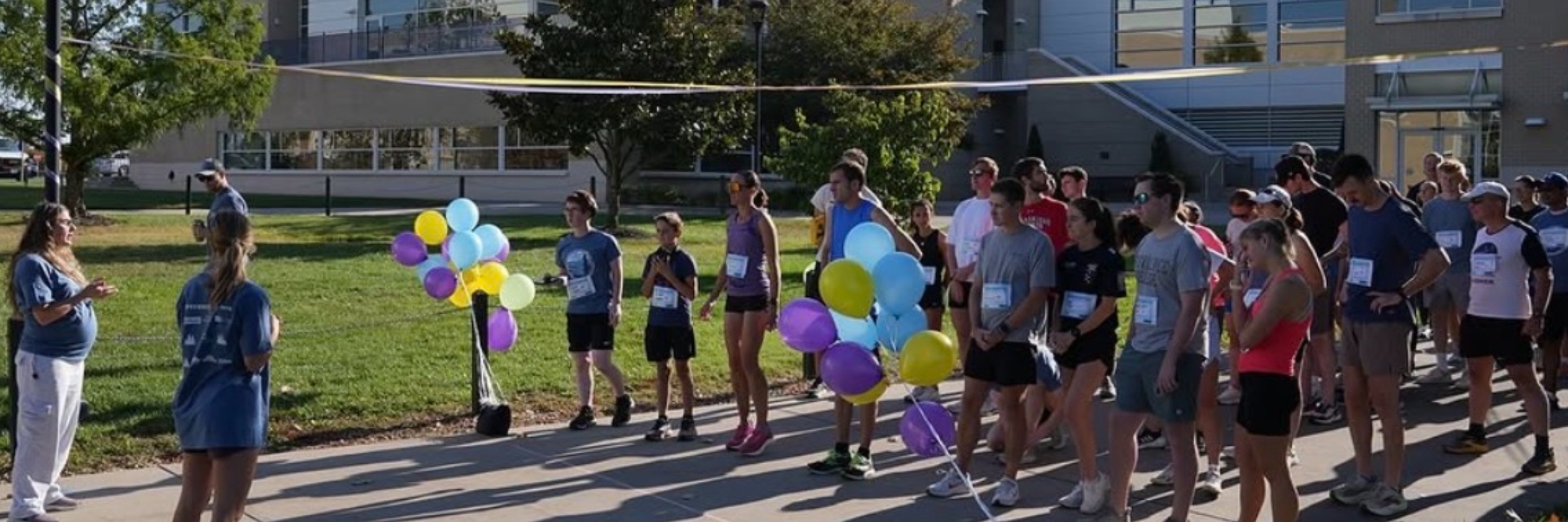 Runners gathered at the start line of the JMU PASS 5K with purple, yellow, and blue balloons